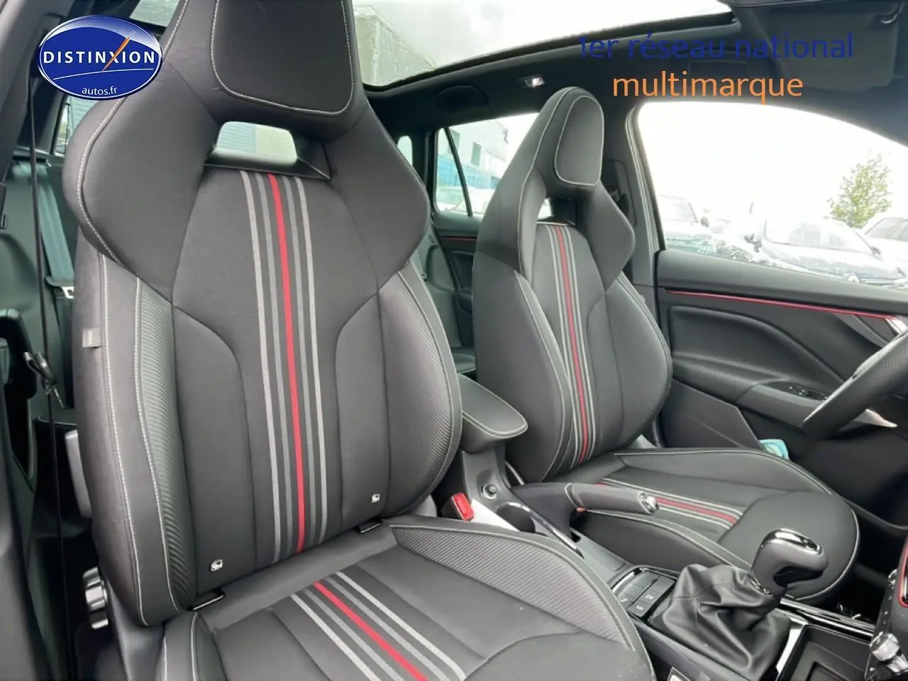 Vue intérieure avant du Skoda Kamiq noir 2026, sièges sport noirs avec bandes rouges et grises, volant cuir multifonction.