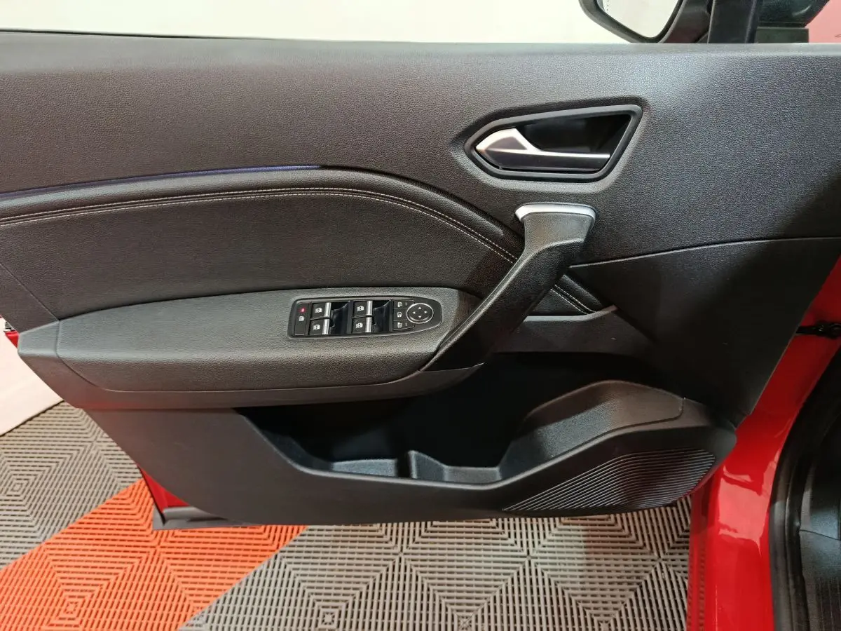 Vue rapprochée de la porte avant gauche noire avec commandes électriques sur un Renault Captur rouge 2024.