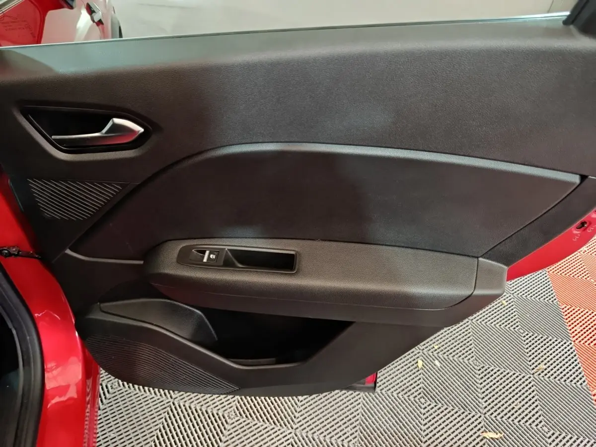 Porte intérieure côté gauche noire avec poignée argentée et bouton de lève-vitre sur Renault Captur rouge 2024.