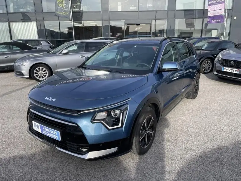 KIA Niro 2024 bleu métal en 3/4 avant droit, avec signature lumineuse distinctive et calandre noire brillante.