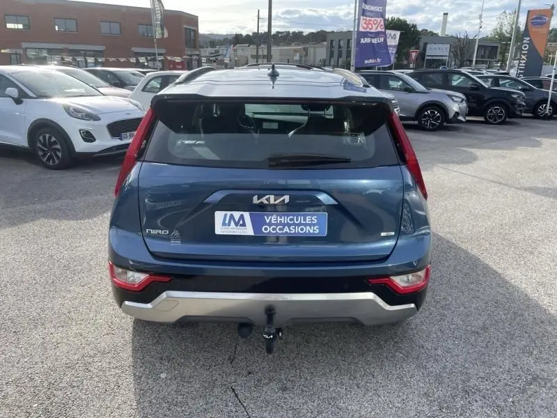 Vue arrière d'un KIA Niro bleu métal 2024 avec attelage, badge hybride et plaque "Véhicules Occasions".