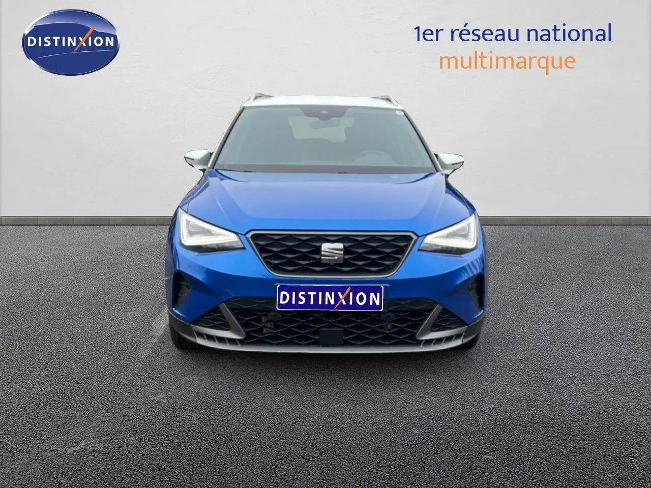 Vue frontale d'un SEAT Arona bleu saphir métal avec toit blanc, calandre noire et phares LED allumés.