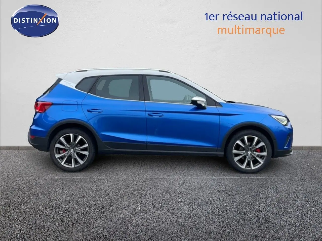 Vue de profil côté gauche d'un SEAT Arona bleu saphir avec toit blanc, roues alliage et étriers rouges visibles.