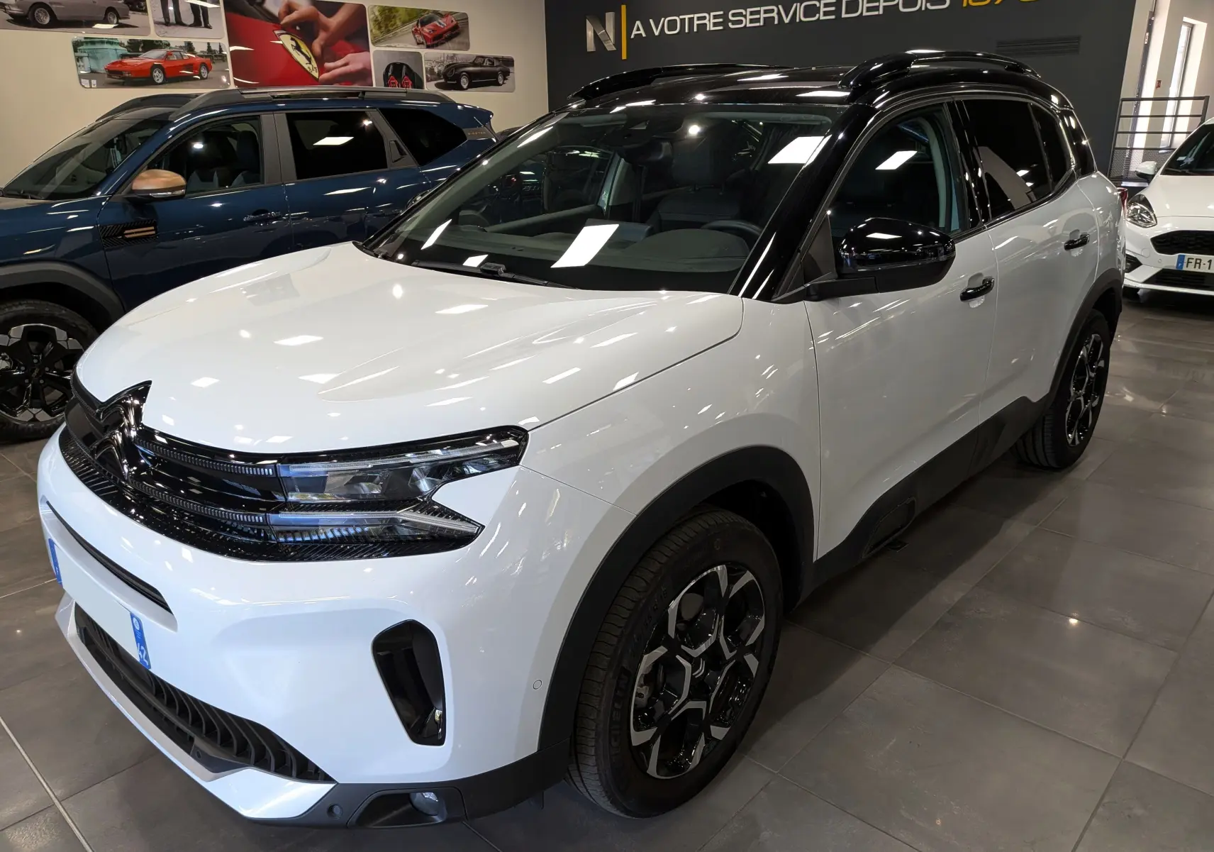 Vue 3/4 avant droite d'un Citroën C5 Aircross 2025 blanc Okénite avec toit noir et jantes noires en concession.