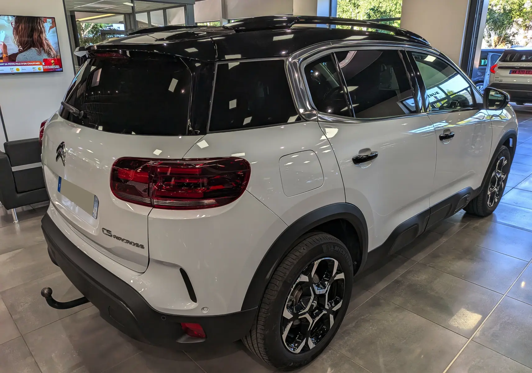 Vue 3/4 arrière droite du Citroën C5 Aircross 2025 blanc Okénite avec toit noir et jantes biton visibles en showroom.