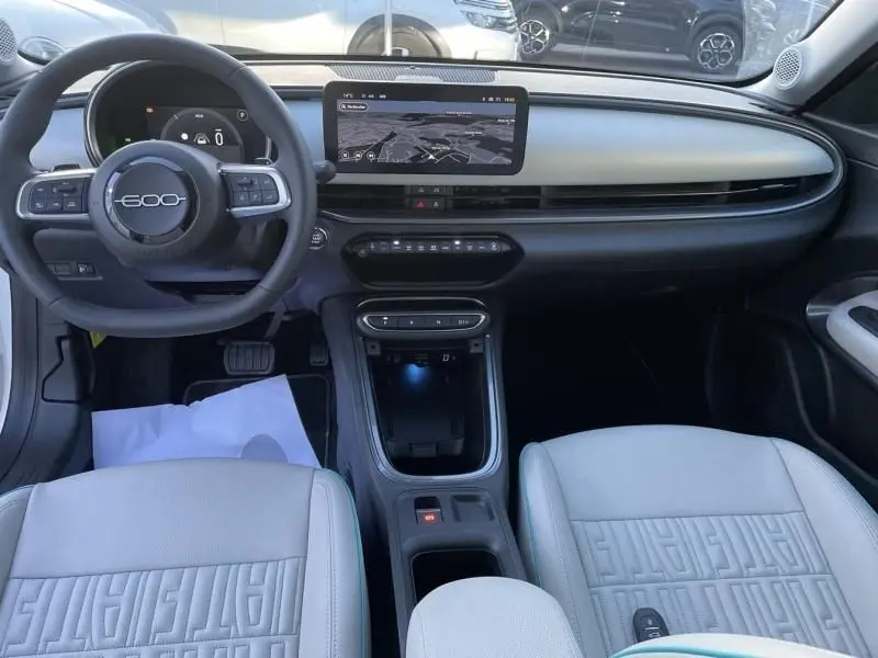 Vue intérieure avant de la Fiat 600 blanche 2025, tableau de bord moderne avec écran tactile central et volant multifonction.