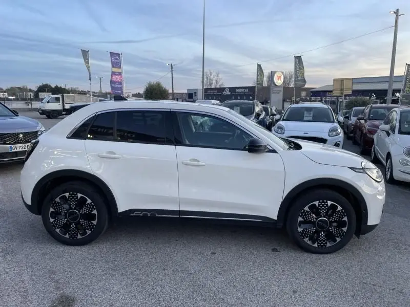 Vue de profil côté gauche d'une FIAT 600 blanche 2025 hybride avec jantes noires à motifs distinctifs.