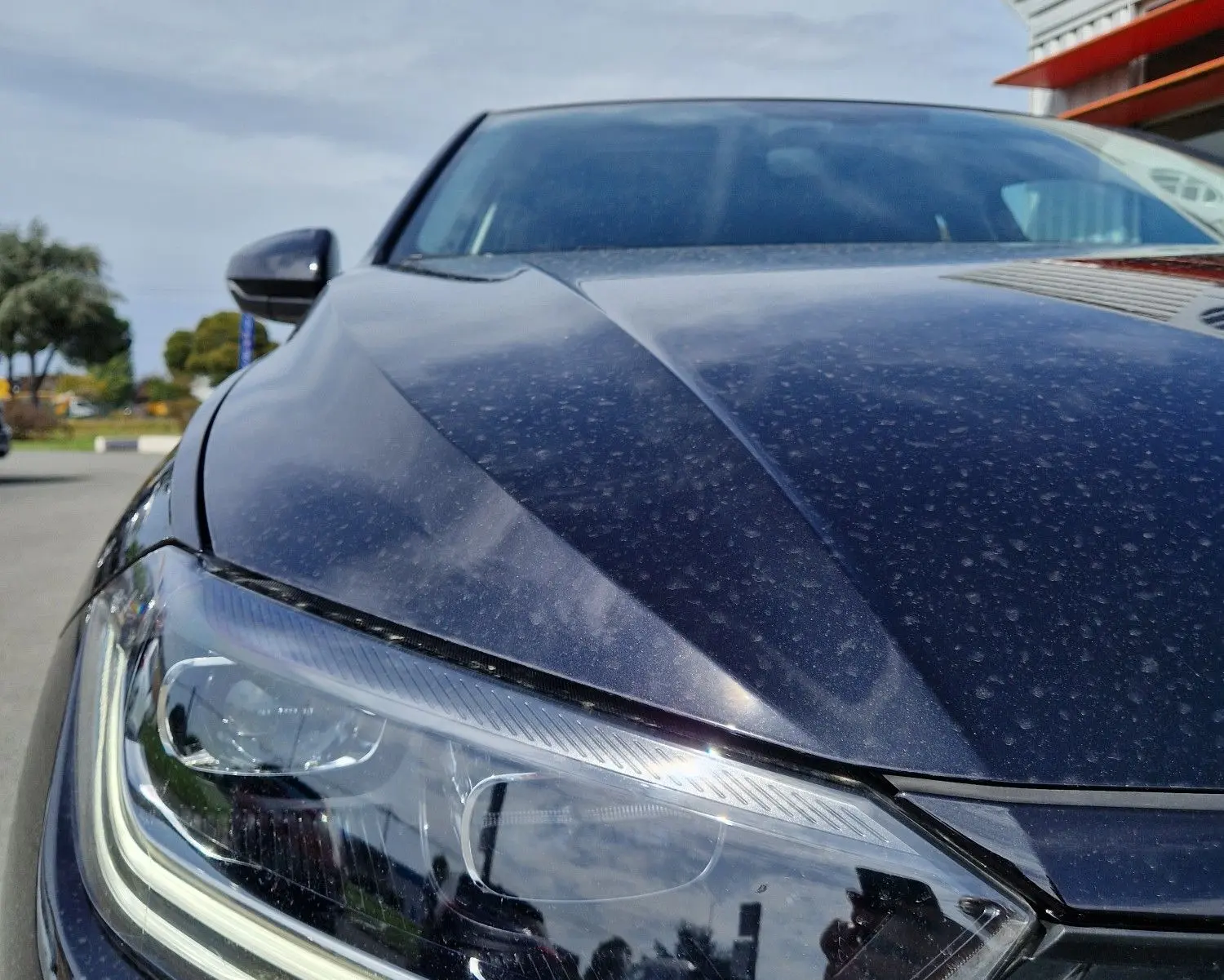 Gros plan sur le phare avant gauche d'une Volkswagen Polo noire 2022, sous un ciel partiellement nuageux.