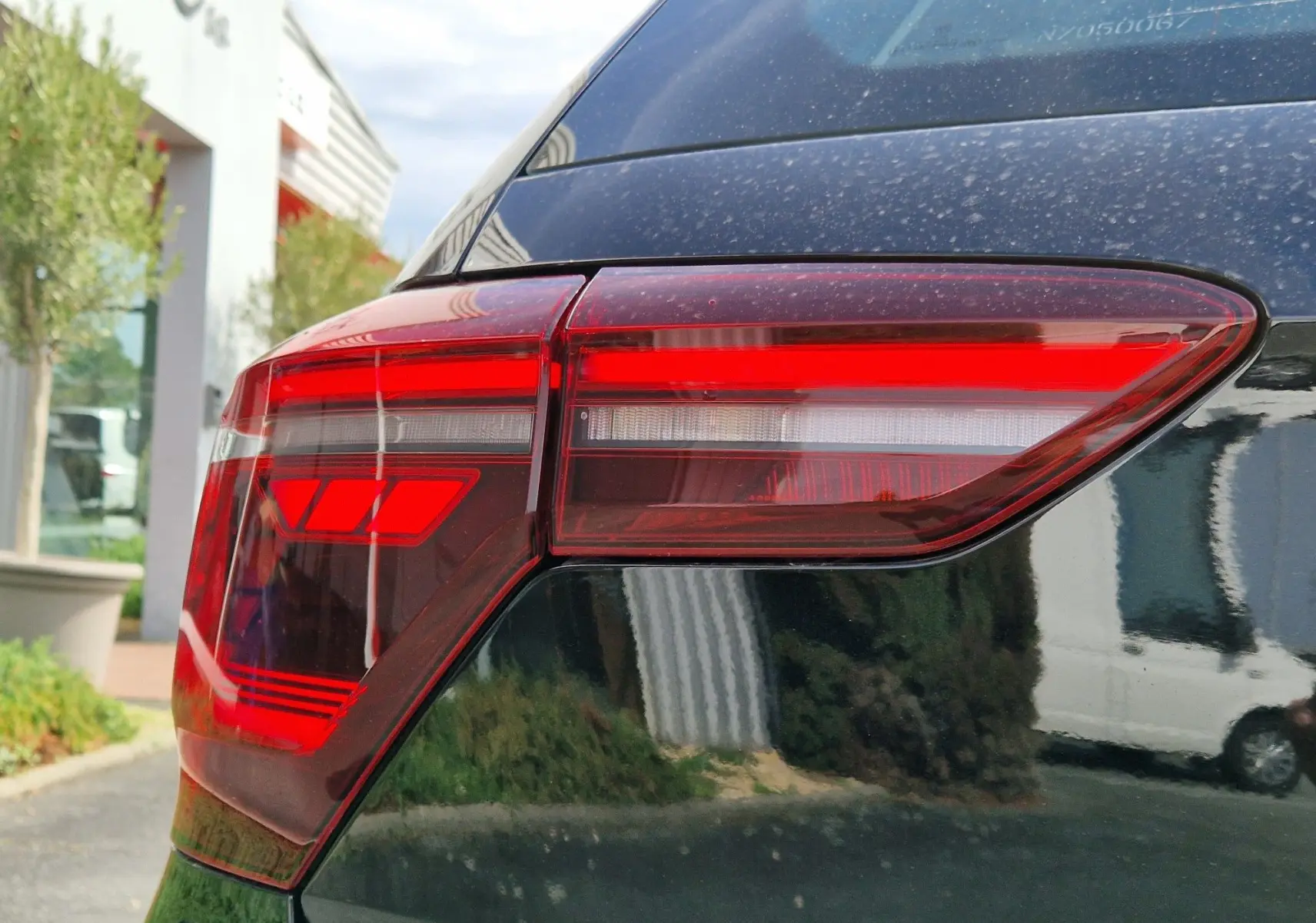 Gros plan sur le feu arrière droit rouge d'une Volkswagen Polo noire 2022, reflet du paysage urbain visible.