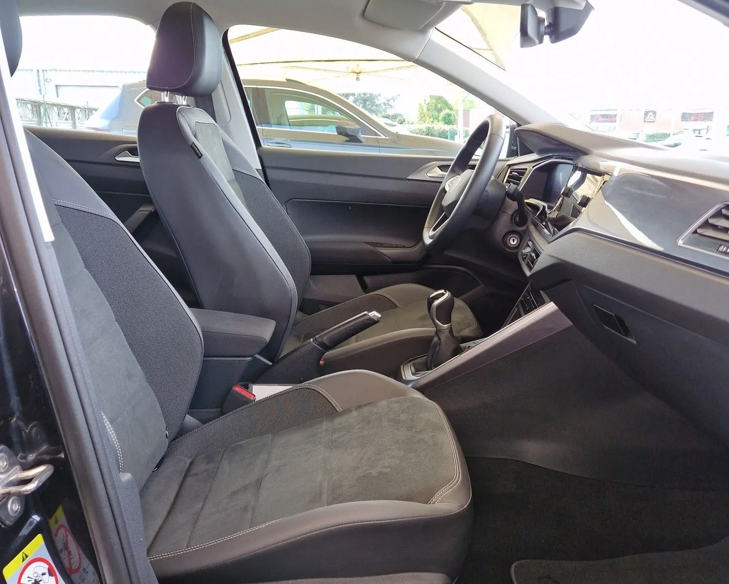 Intérieur côté conducteur d'une Volkswagen Polo noire 2022, sièges tissu noir et toit ouvrant panoramique visible.