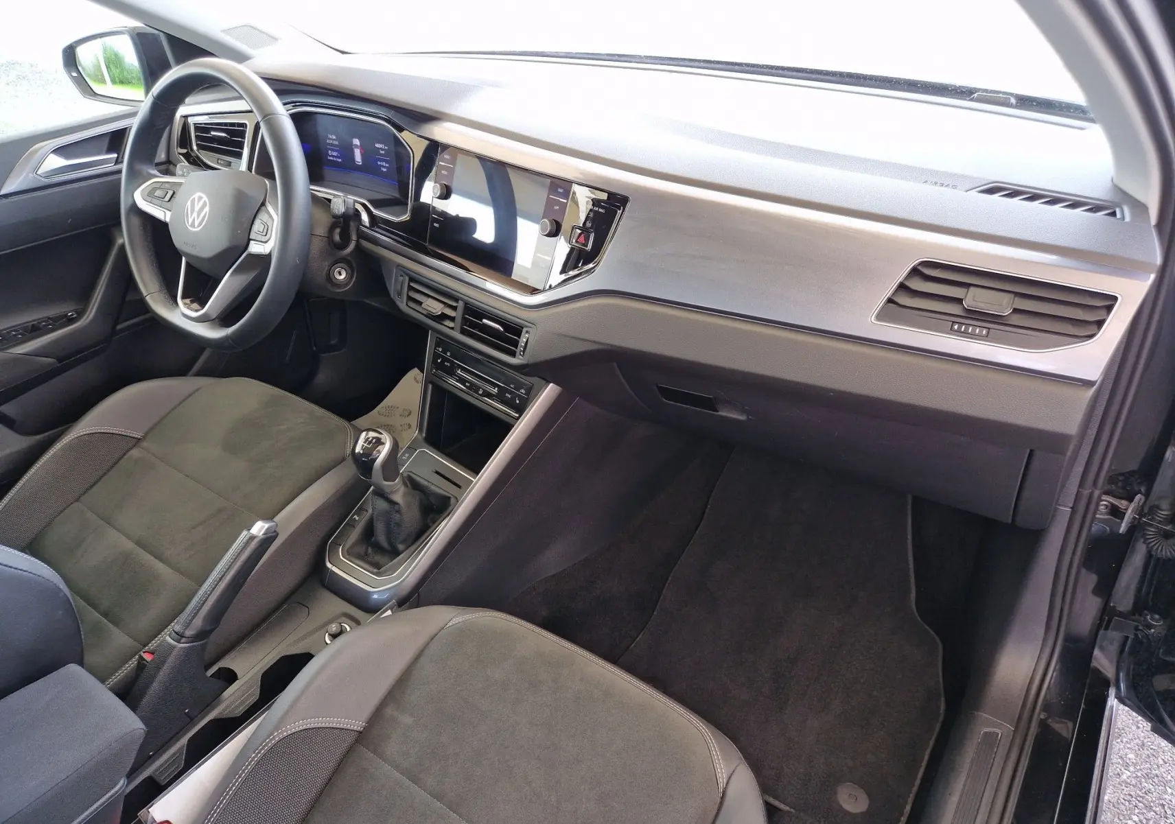 Intérieur côté conducteur d'une Volkswagen Polo noire 2022, avec tableau de bord moderne et boîte manuelle visible.