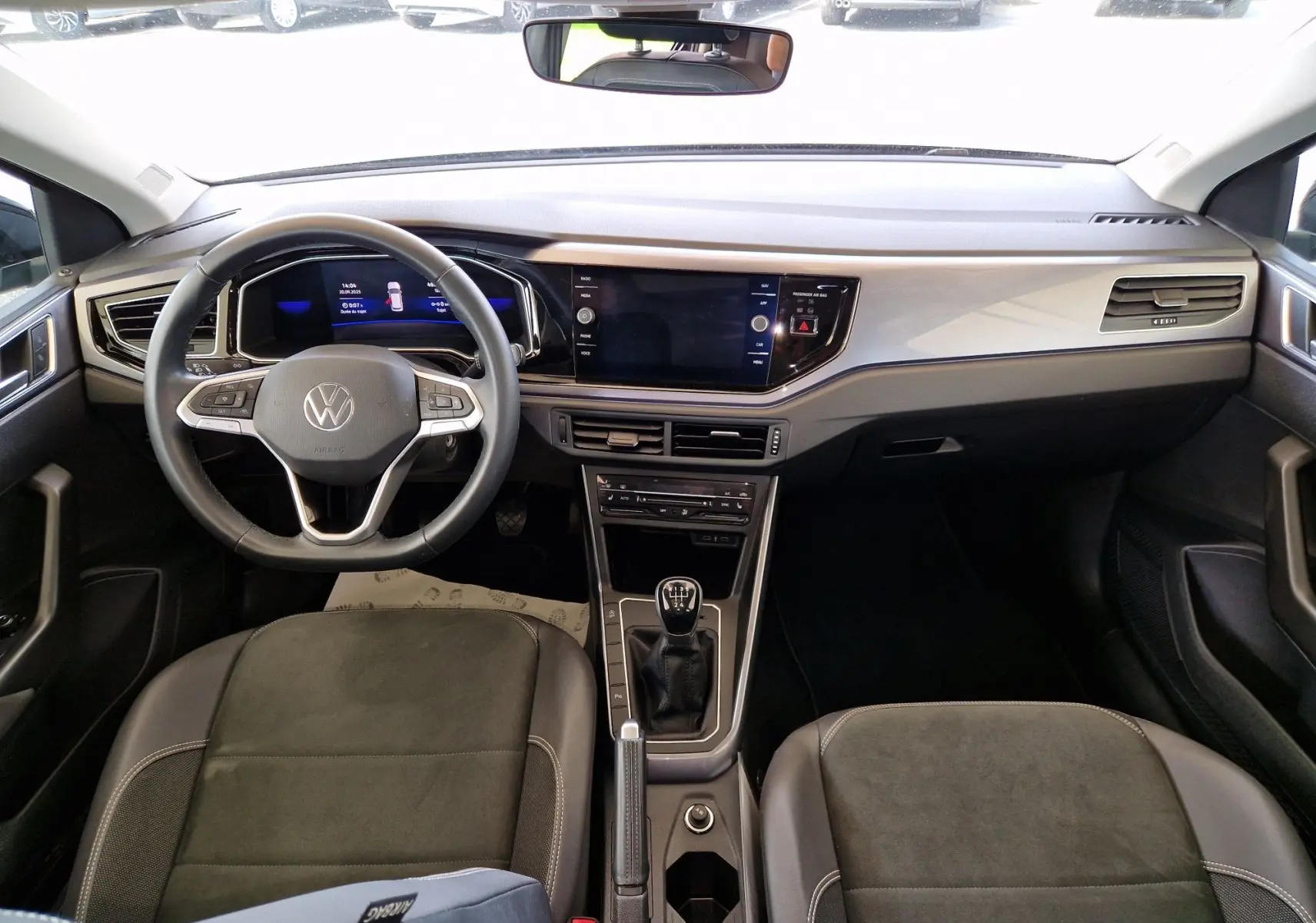 Intérieur de la Volkswagen Polo noire 2022, vue frontale du tableau de bord avec volant multifonction et boîte manuelle.