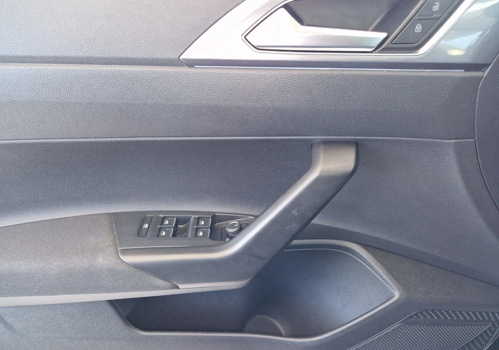 Vue rapprochée de la porte côté gauche d'une Volkswagen Polo noire 2022, montrant les commandes des vitres et la poignée intérieure.