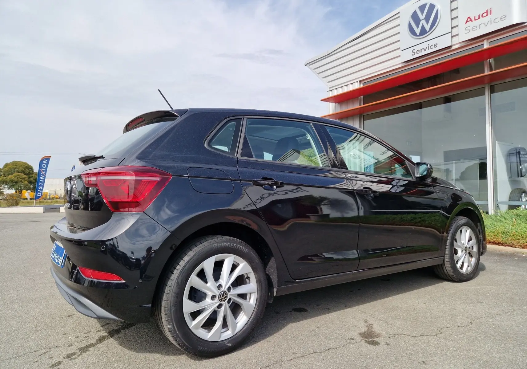 Volkswagen Polo noire vue de trois quarts arrière droit, stationnée devant un service Volkswagen et Audi.