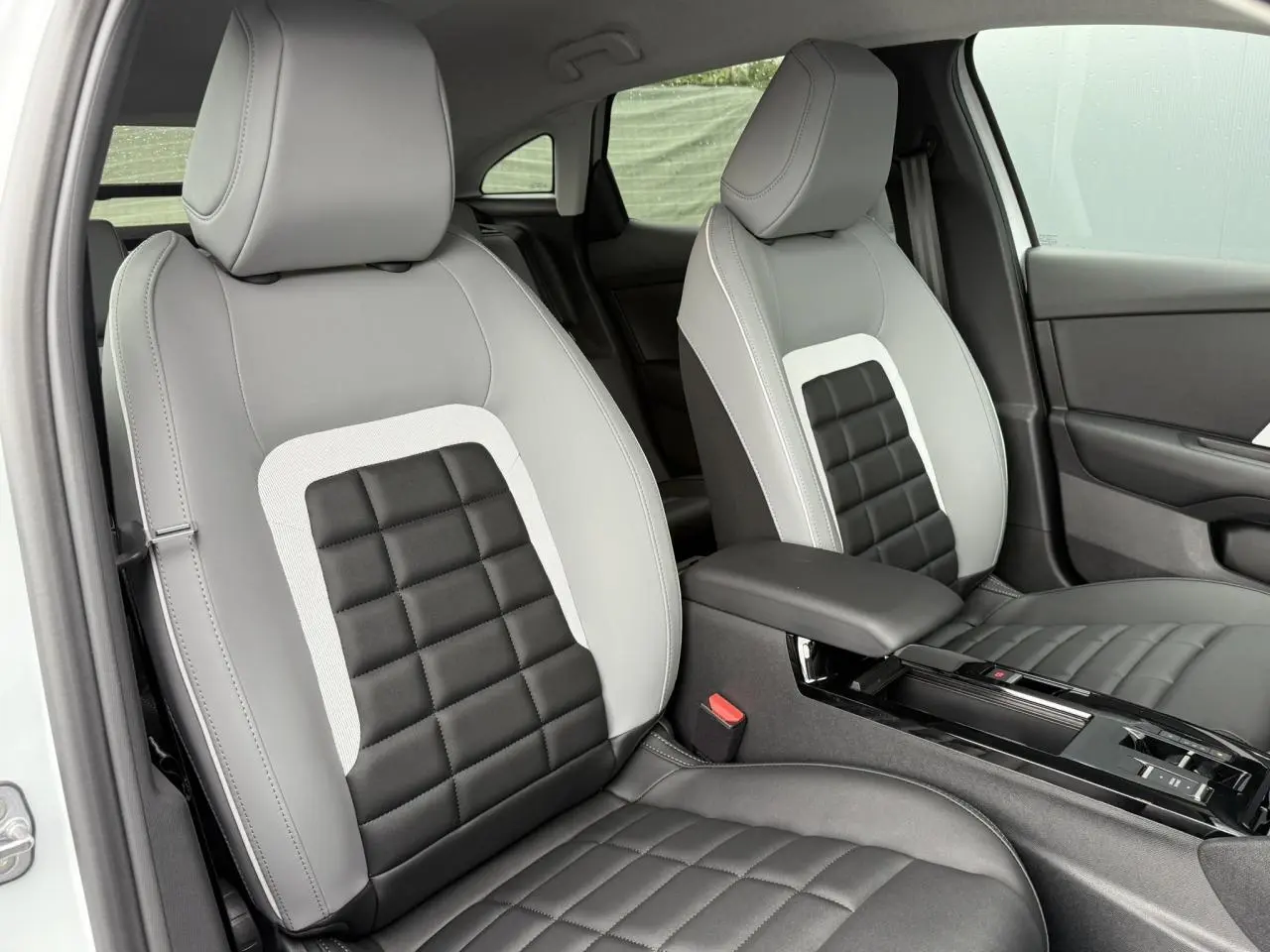 Vue rapprochée des sièges avant gris clair et noir matelassé de la Citroën C4 NV Hybrid 2025, avec accoudoir central.