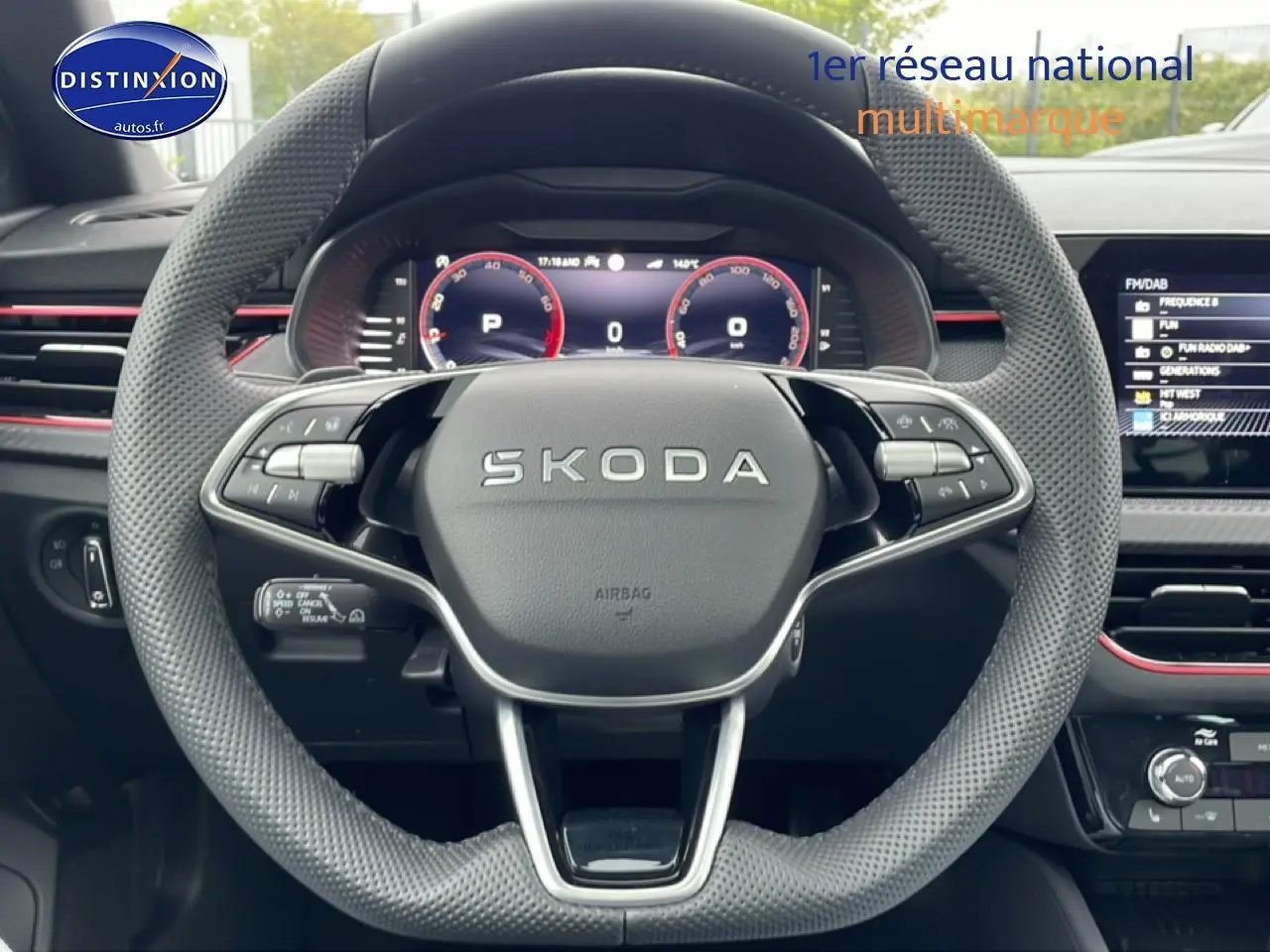 Vue centrée sur le volant perforé SKODA avec tableau de bord numérique et touches multifonctions, ambiance intérieure noire avec touches rouges.