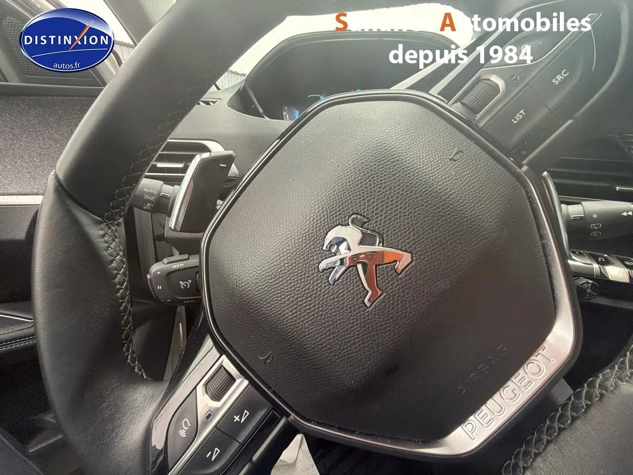 Gros plan sur le volant cuir noir du Peugeot 3008 Hybrid 2021 avec logo lion chromé et commandes intégrées.