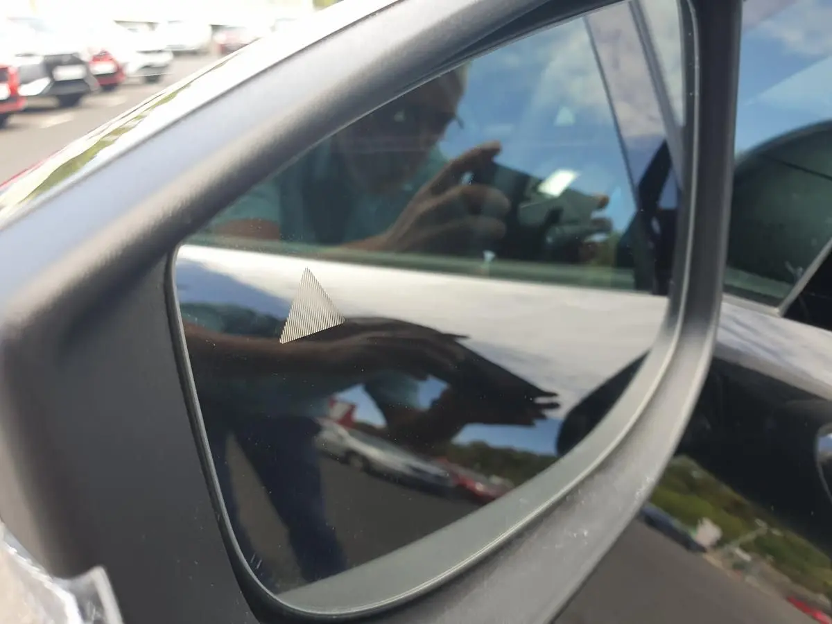 Rétroviseur côté gauche d’une Renault Clio VI noire étoile, reflétant partiellement l’environnement extérieur.