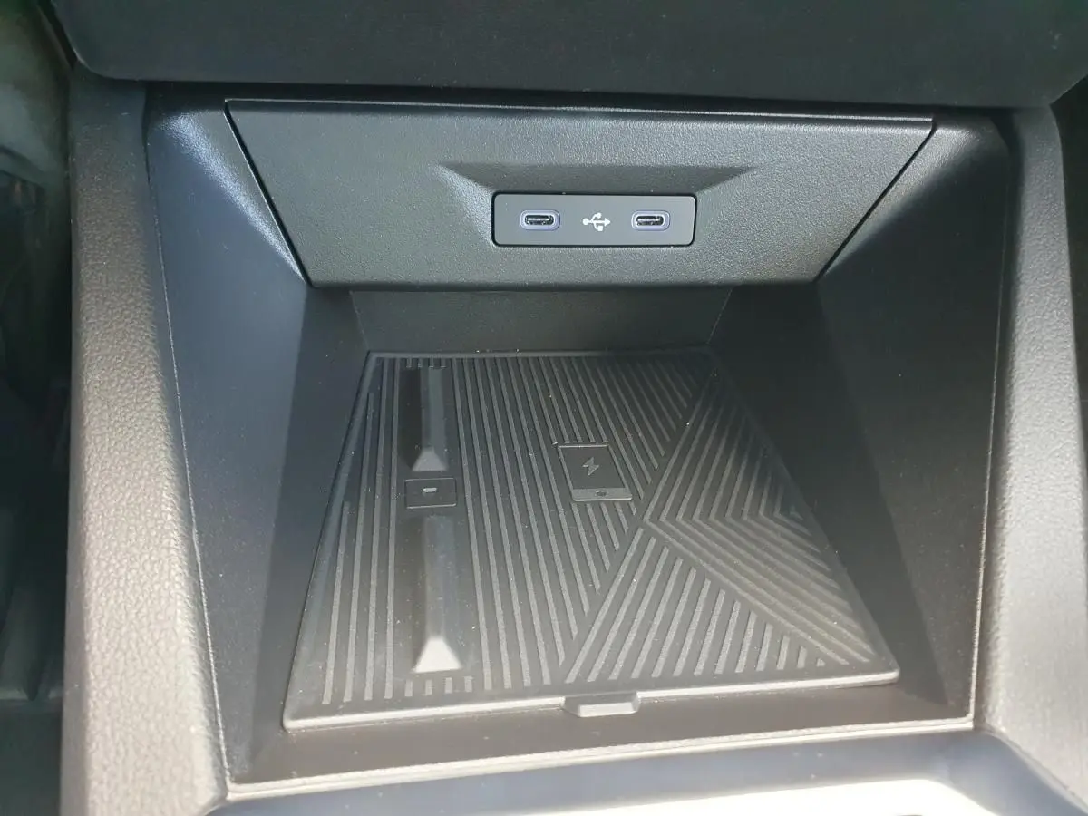 Vue rapprochée du rangement central avant de la Renault Clio VI noire étoile, avec deux prises USB-C et chargeur sans fil intégré.