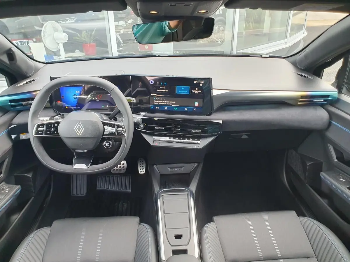 Vue intérieure avant du tableau de bord et volant de la Renault Clio VI noire étoile avec écran tactile panoramique et finitions bleues.