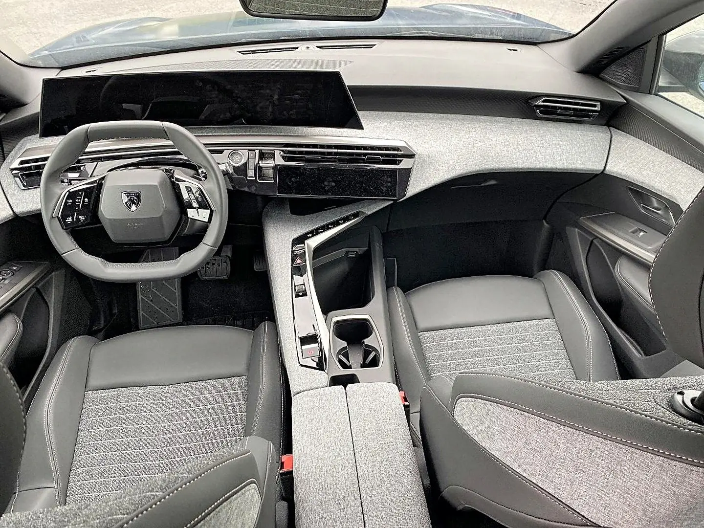 Vue intérieure avant du Peugeot 3008 2025, avec tableau de bord moderne et sièges gris tissu et cuir.