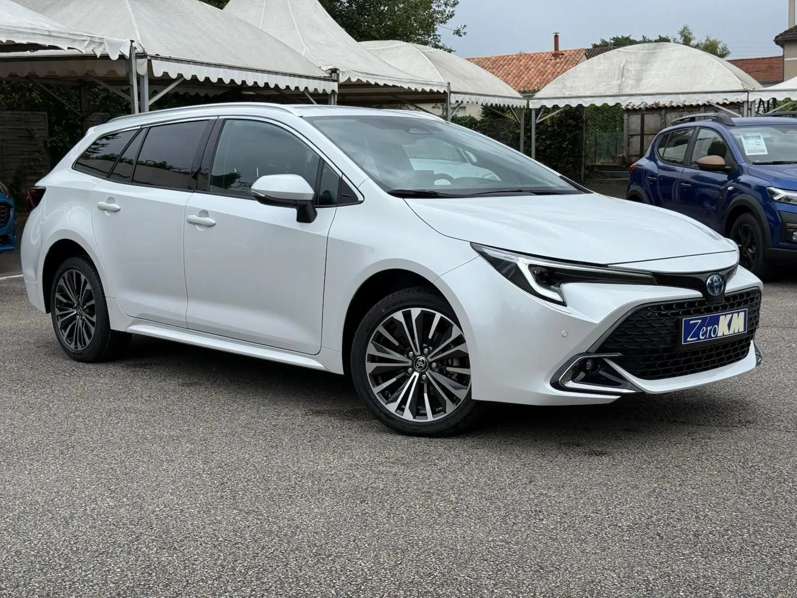 Toyota Corolla Touring Sport blanche nacrée vue en 3/4 avant côté gauche, avec jantes alliage et calandre noire distinctive.