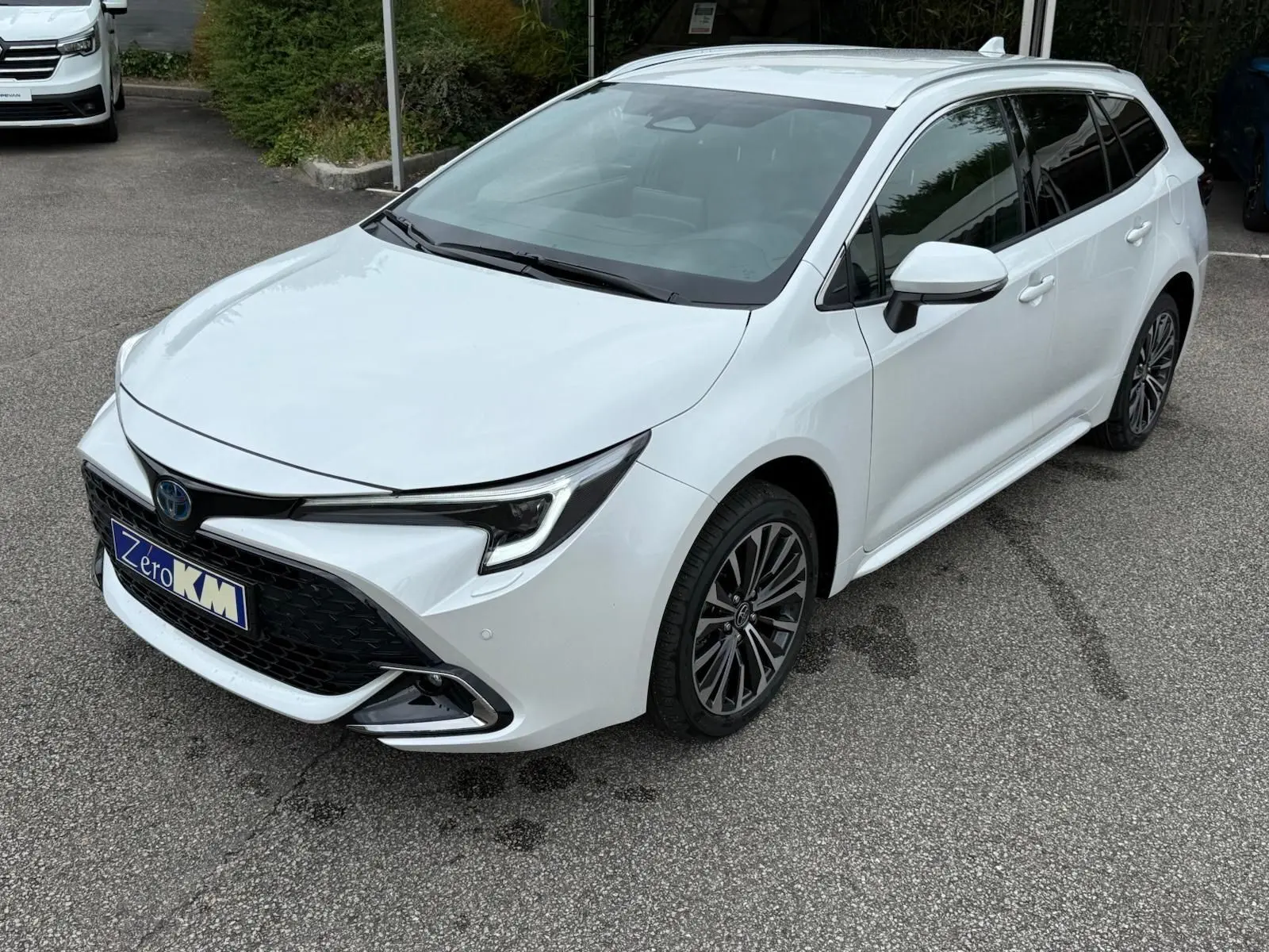 Toyota Corolla Touring Sport blanche nacrée vue en 3/4 avant droit, avec calandre noire et jantes alliage foncé.