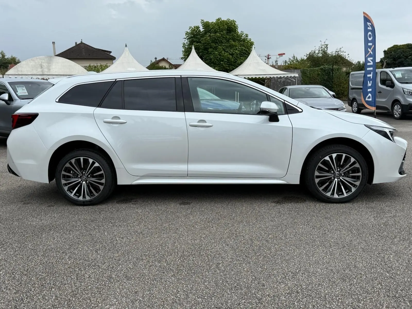 Profil côté gauche d'une Toyota Corolla Touring Sport blanche lunaire nacrée, avec jantes alliage et vitres teintées.