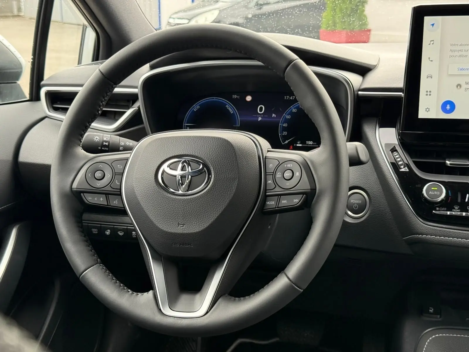 Vue centrée sur le volant noir de la Toyota Corolla Touring Sport 2025, avec tableau de bord numérique et écran tactile visible.
