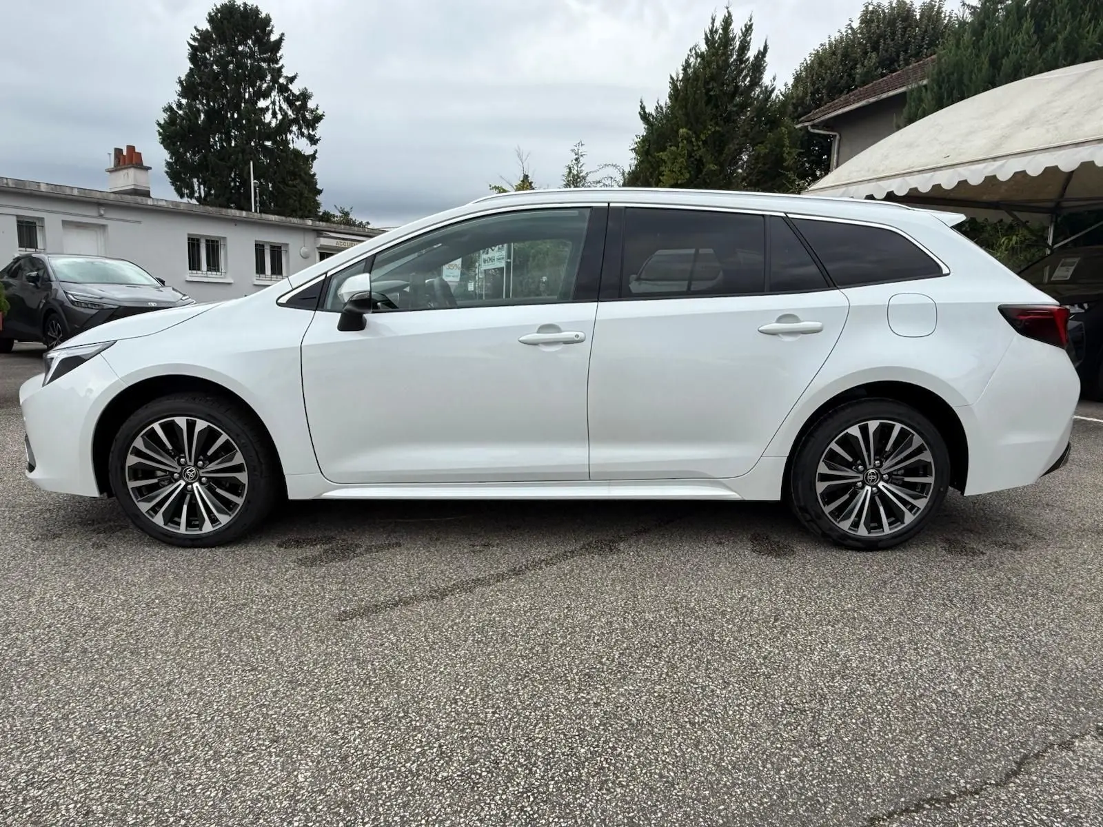 Profil côté gauche d'une Toyota Corolla Touring Sport 2025 blanc lunaire nacré avec jantes alliage noires et grises.