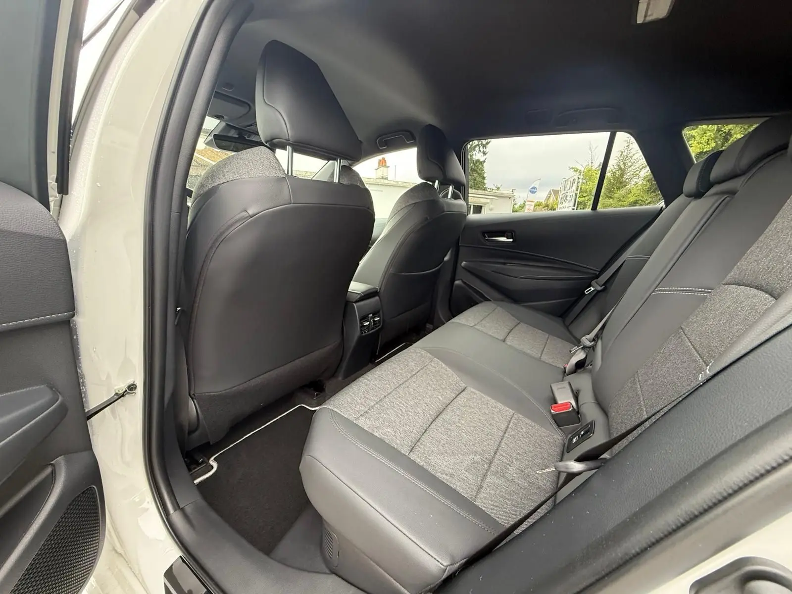 Vue intérieure arrière droite de la Toyota Corolla Touring Sport 2025 blanc lunaire nacré, sièges bi-matière gris et noir.