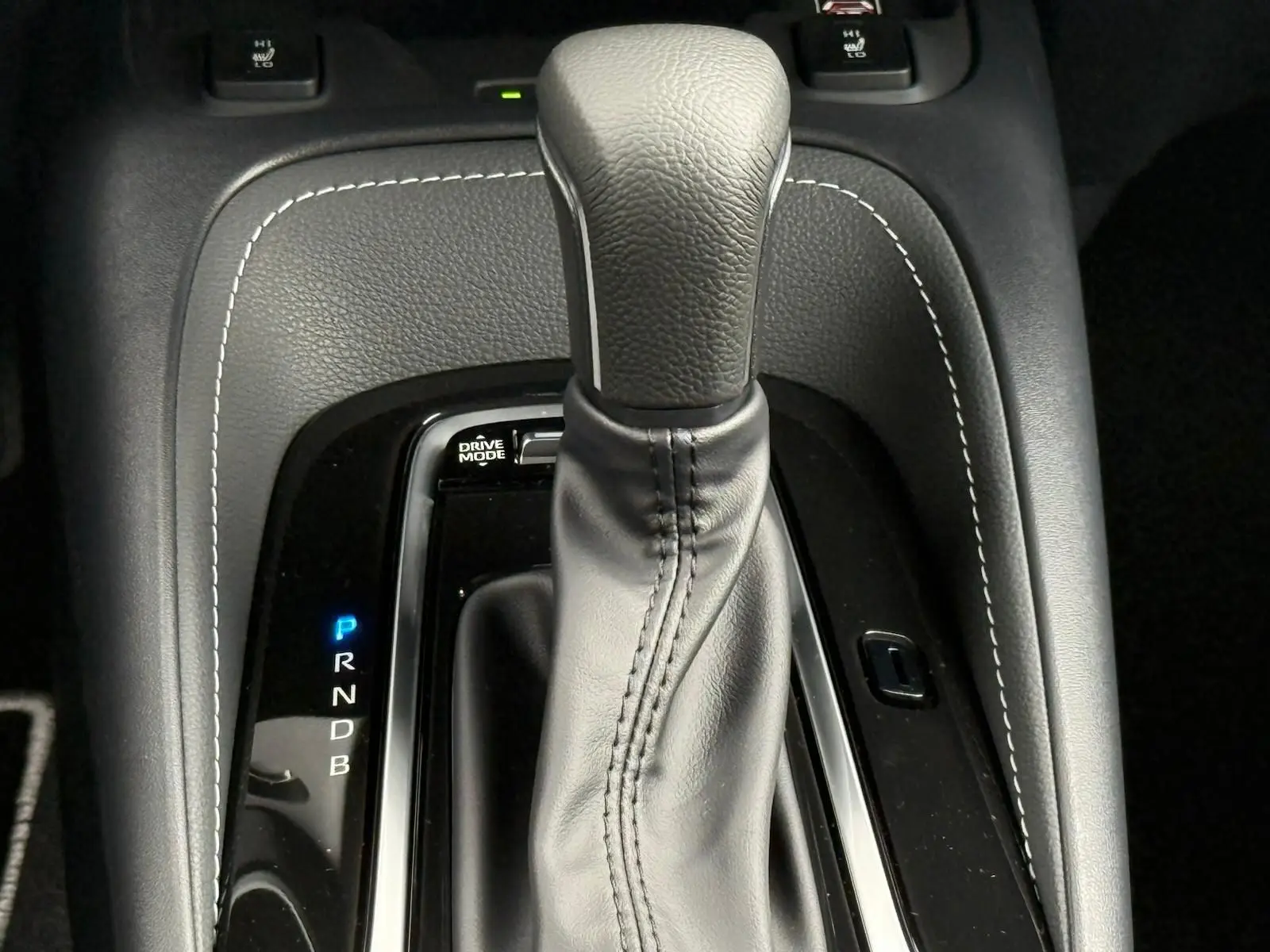 Gros plan sur le levier de vitesses automatique en cuir noir avec surpiqûres blanches de la Toyota Corolla Touring Sport blanche.