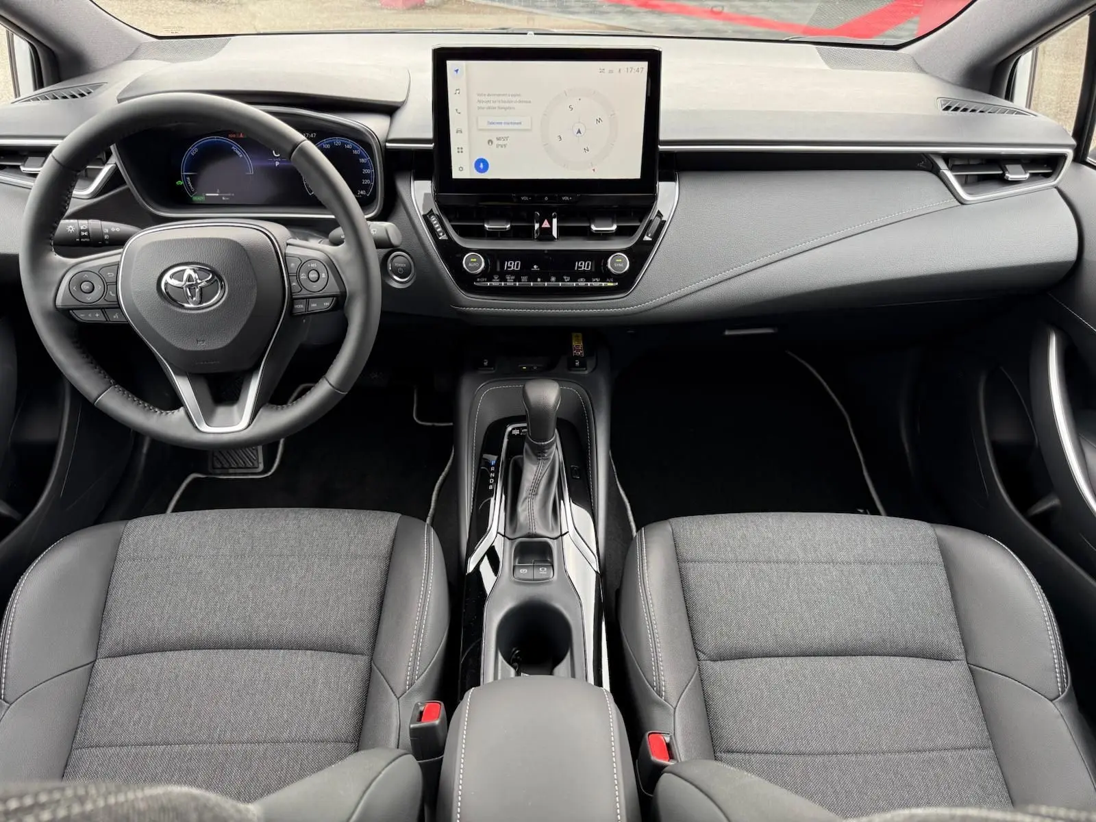 Vue intérieure frontale de la Toyota Corolla Touring Sport 2025, tableau de bord moderne avec écran tactile et sièges gris tissu et cuir.
