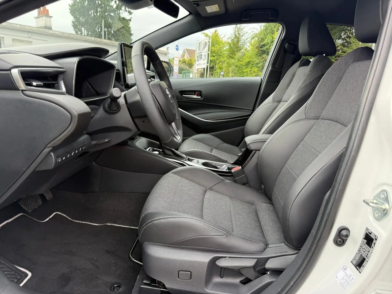 Intérieur de la Toyota Corolla Touring Sport 2025 vue côté conducteur, sièges gris tissu et cuir, tableau de bord moderne.