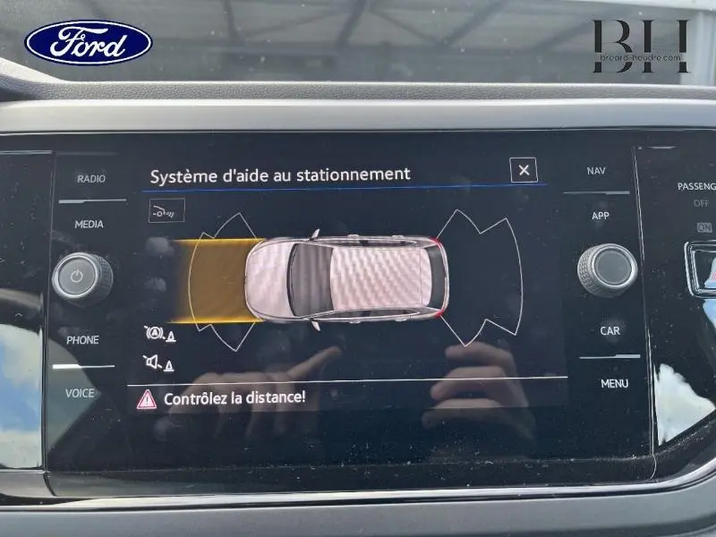 Écran tactile du système d'aide au stationnement montrant une Volkswagen Polo argentée vue de dessus avec alerte de distance.