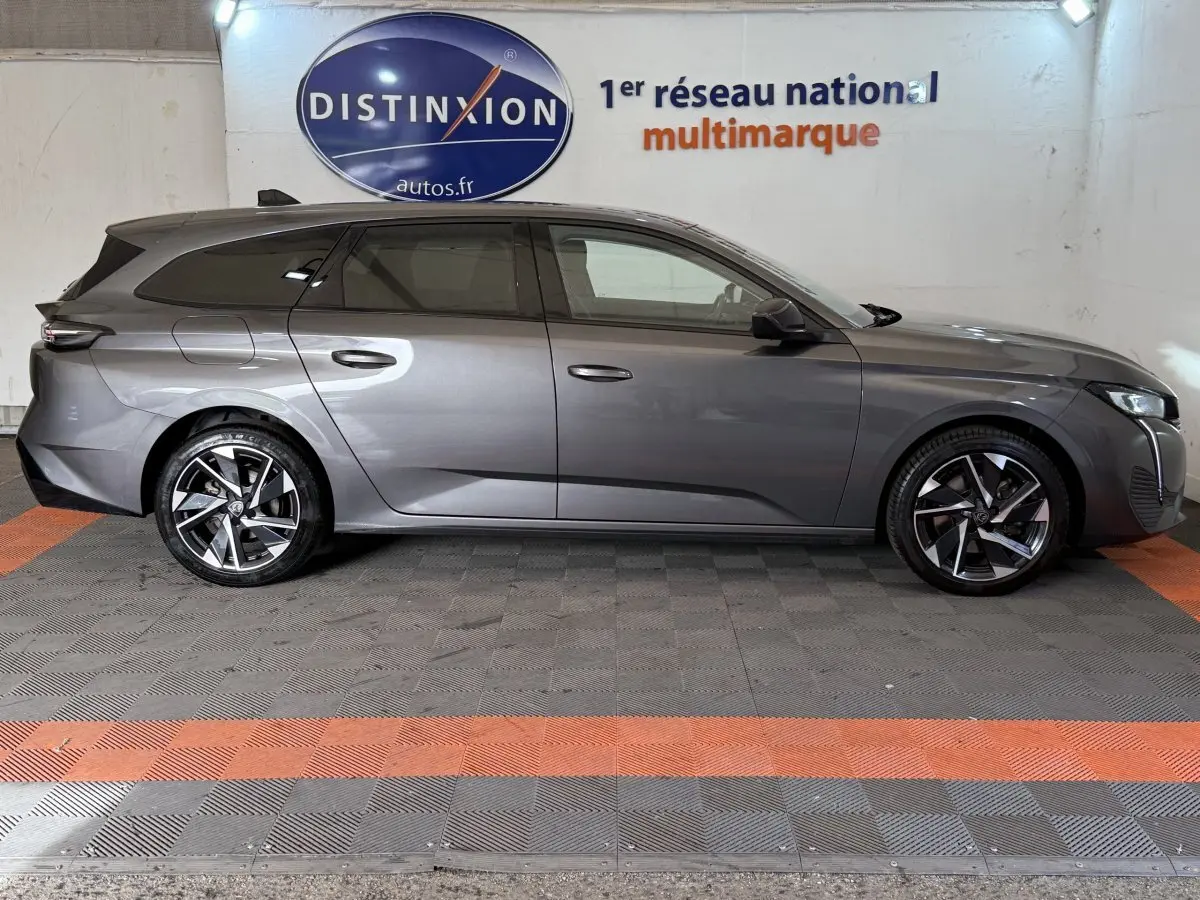 Peugeot 308 SW gris foncé vue de profil côté gauche, avec jantes alliage et toit noir en arrière-plan intérieur showroom.