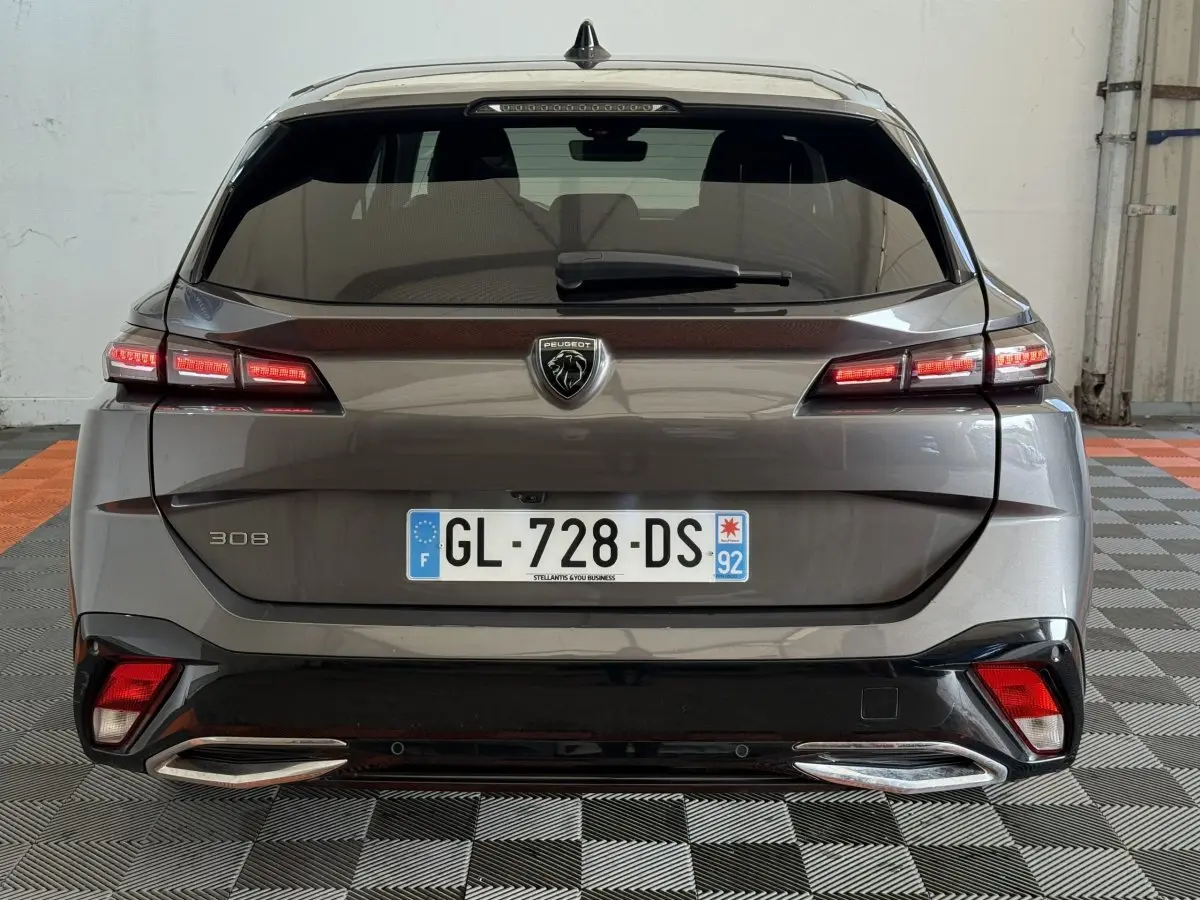 Vue arrière d'une Peugeot 308 gris foncé avec feux LED allumés et double sortie d'échappement chromée.