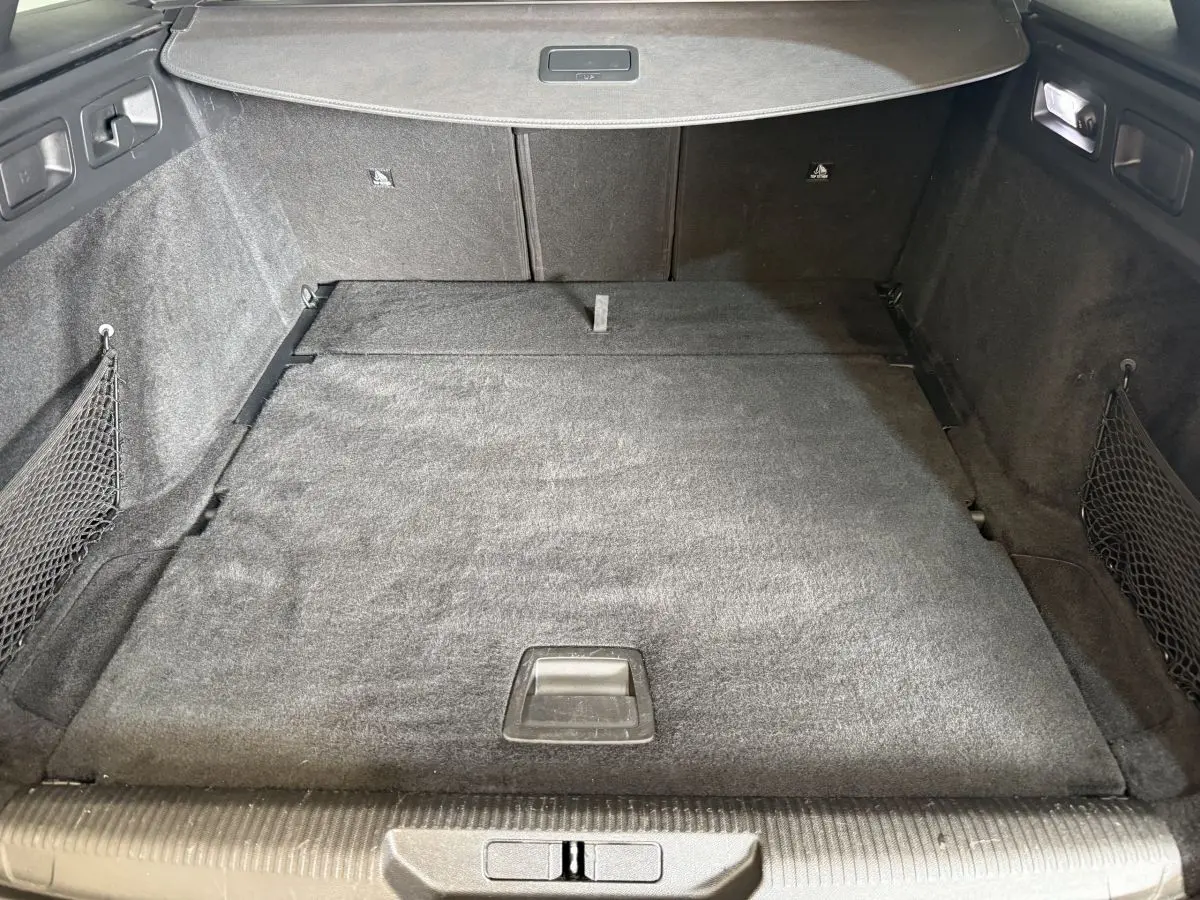 Vue intérieure du coffre spacieux et plat de la Peugeot 308 SW gris foncé, avec filet de rangement latéral et éclairage intégré.