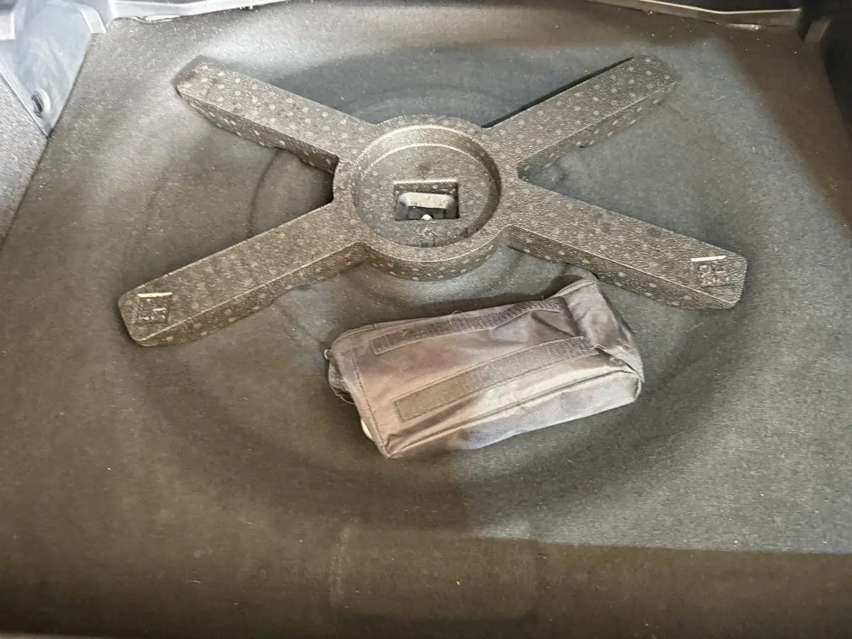 Vue rapprochée du coffre d’une Peugeot 308 gris foncé, montrant un rangement avec une trousse noire posée dessus.