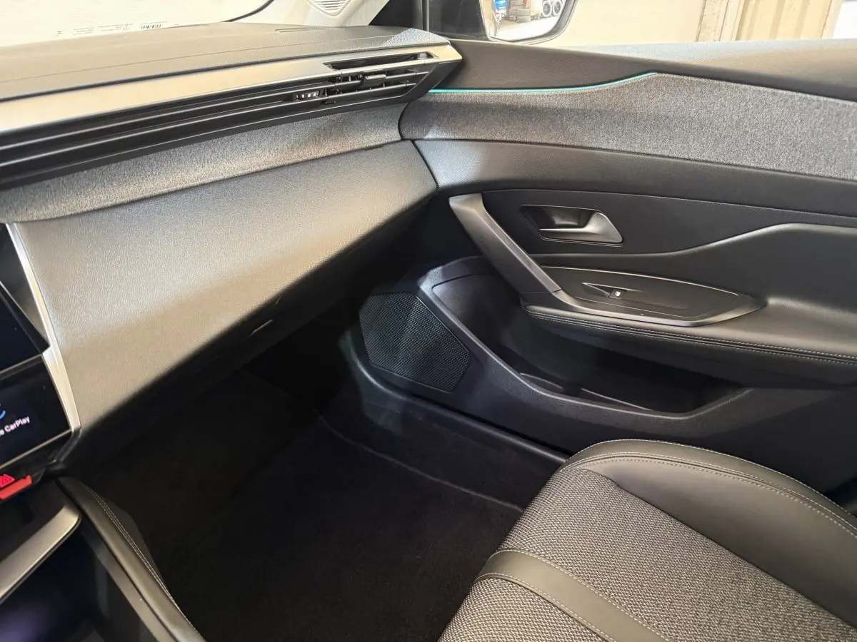 Vue intérieure côté passager avant du Peugeot 308 gris foncé, mettant en valeur la porte et la console épurée.