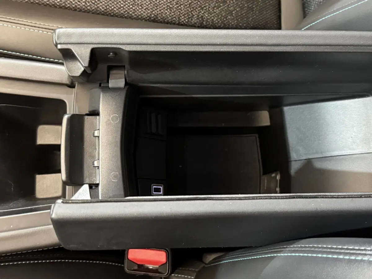 Vue intérieure en plongée sur le rangement central ouvert d'une Peugeot 308 SW gris foncé, avec coutures bleues visibles sur le siège.