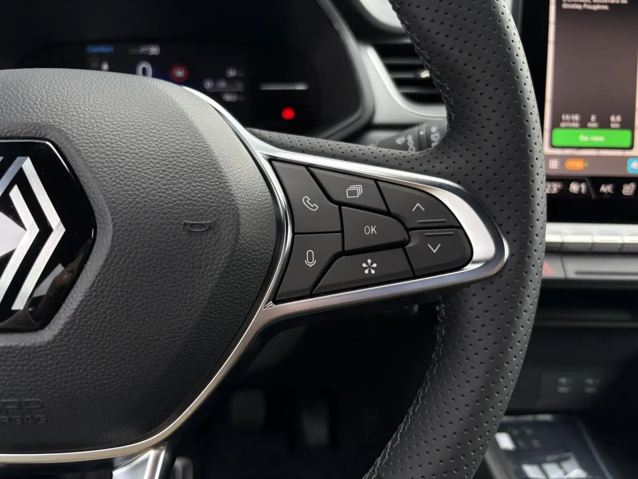 Gros plan sur le volant noir perforé du Renault Captur 2025 avec commandes intégrées et écran tactile en arrière-plan.