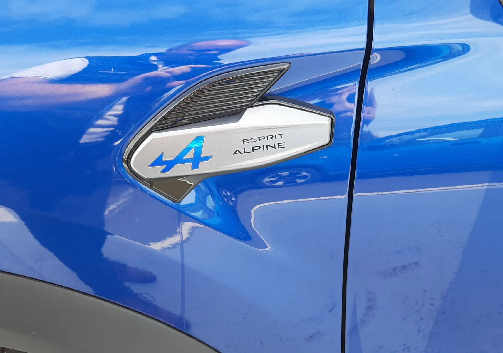 Gros plan sur l'emblème Esprit Alpine côté gauche d'un Renault Captur bleu iron avec toit noir.