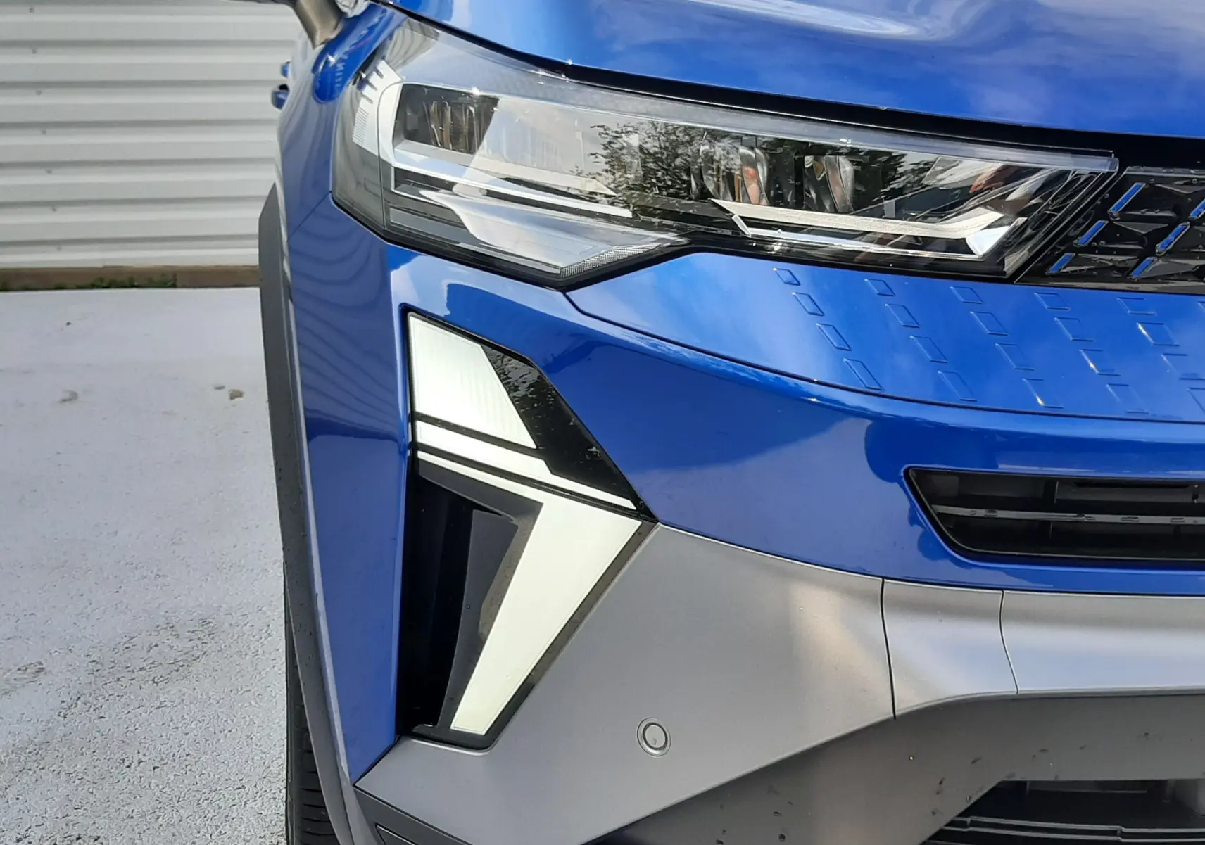 Gros plan sur l'avant gauche du Renault Captur 2024 bleu Iron avec feux LED au design angulaire et calandre noire.