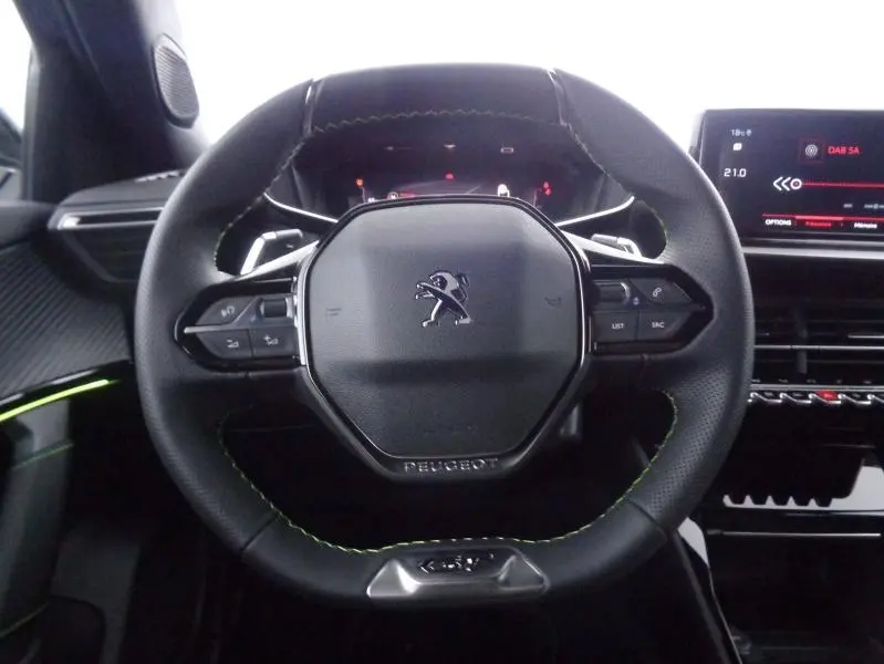 Gros plan sur le volant cuir noir avec surpiqûres vertes du Peugeot 2008 2023, tableau de bord et écran tactile en arrière-plan.