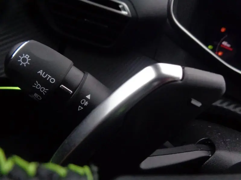 Gros plan sur la commande des phares et le levier de vitesse au volant du Peugeot 2008 gris Artense, intérieur sombre.