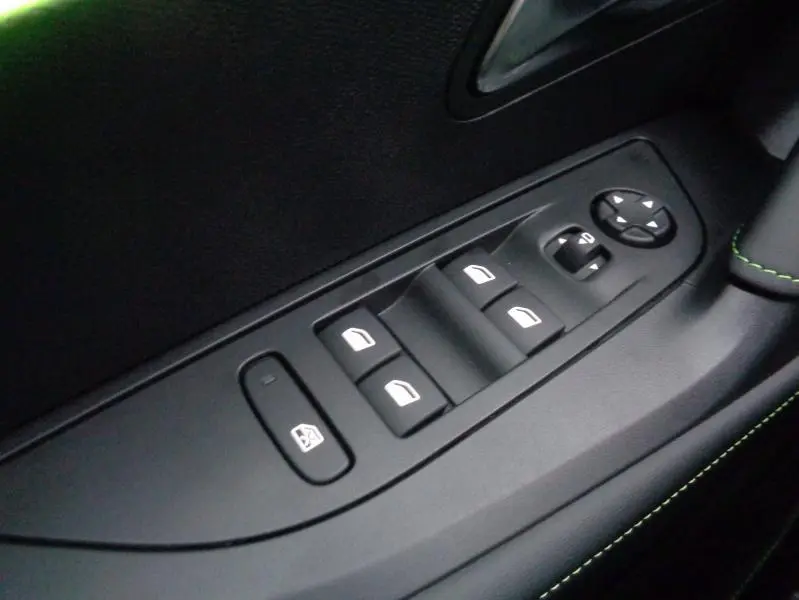 Gros plan sur les commandes des vitres électriques côté conducteur du Peugeot 2008 gris Artense avec surpiqûres vertes.