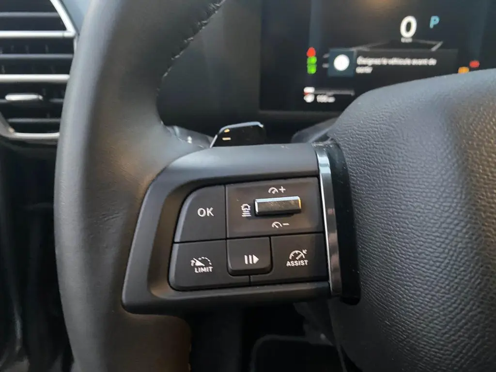 Gros plan sur les commandes multifonctions gauche du volant noir d'une Citroën C4 2025, avec affichage numérique en arrière-plan.
