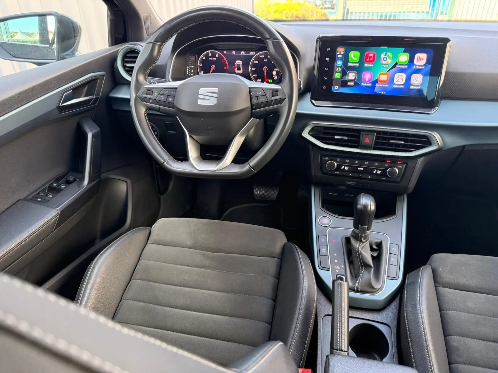 Intérieur du SEAT Arona 2022 vu de face, volant cuir, écran tactile central avec Apple CarPlay, sièges tissu noir.