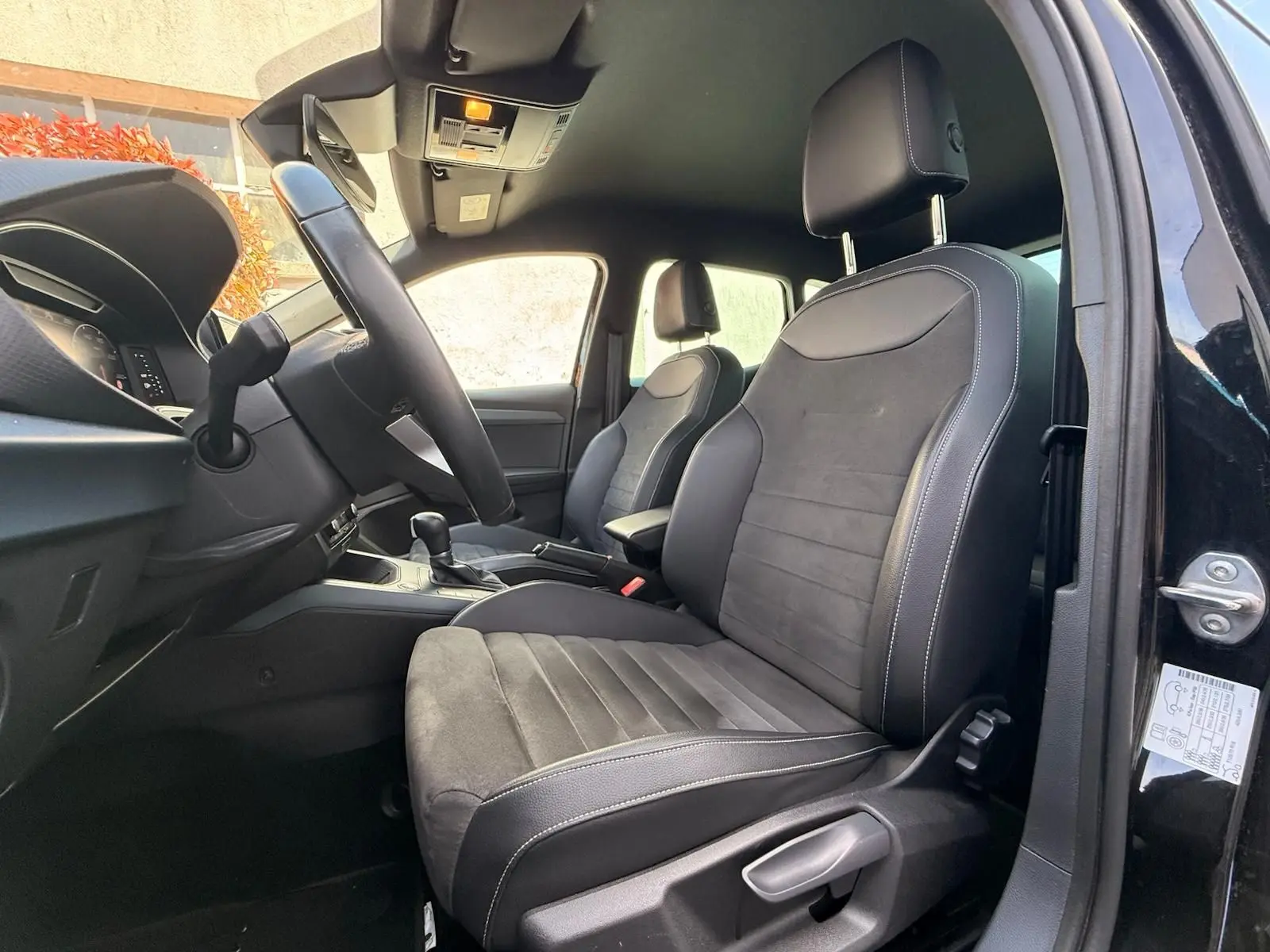 Vue intérieure côté conducteur de la SEAT Arona 2022 avec sièges noirs en tissu et cuir, volant multifonctions visible.